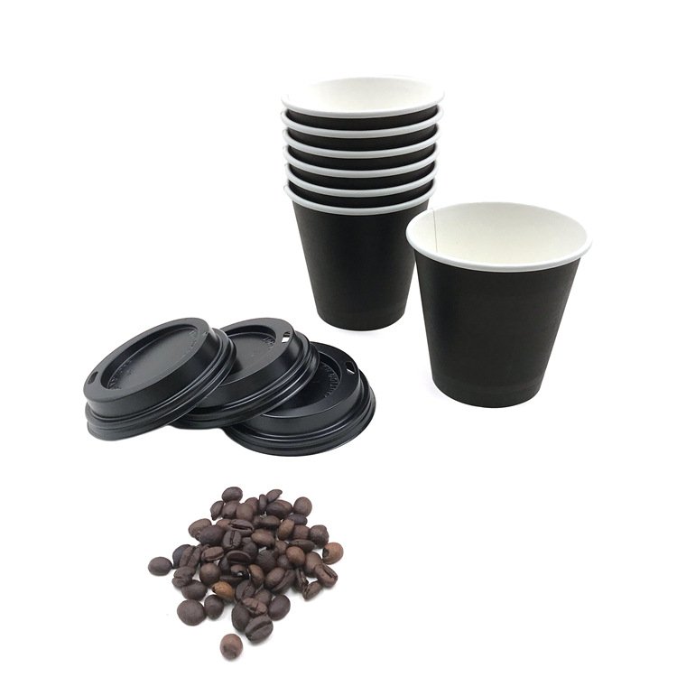 Black paper cups with lids and coffee beans arranged as a coffee service setting