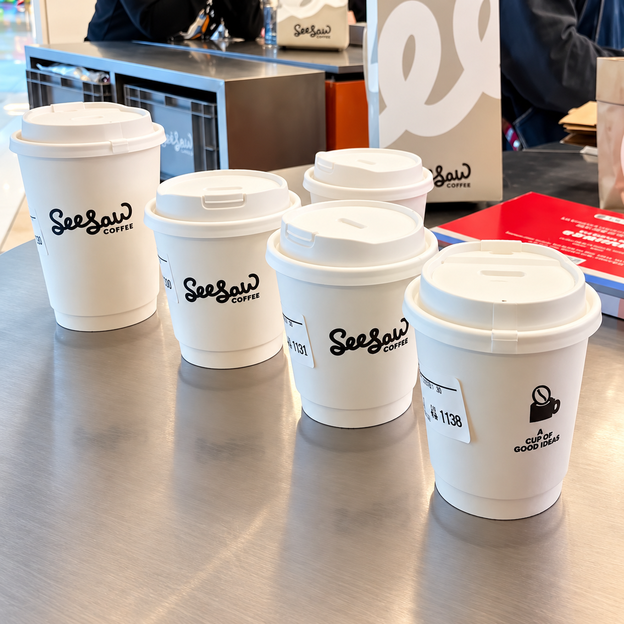 Branded paper cups with lids on a cafe counter showing finished printed cup configuration
