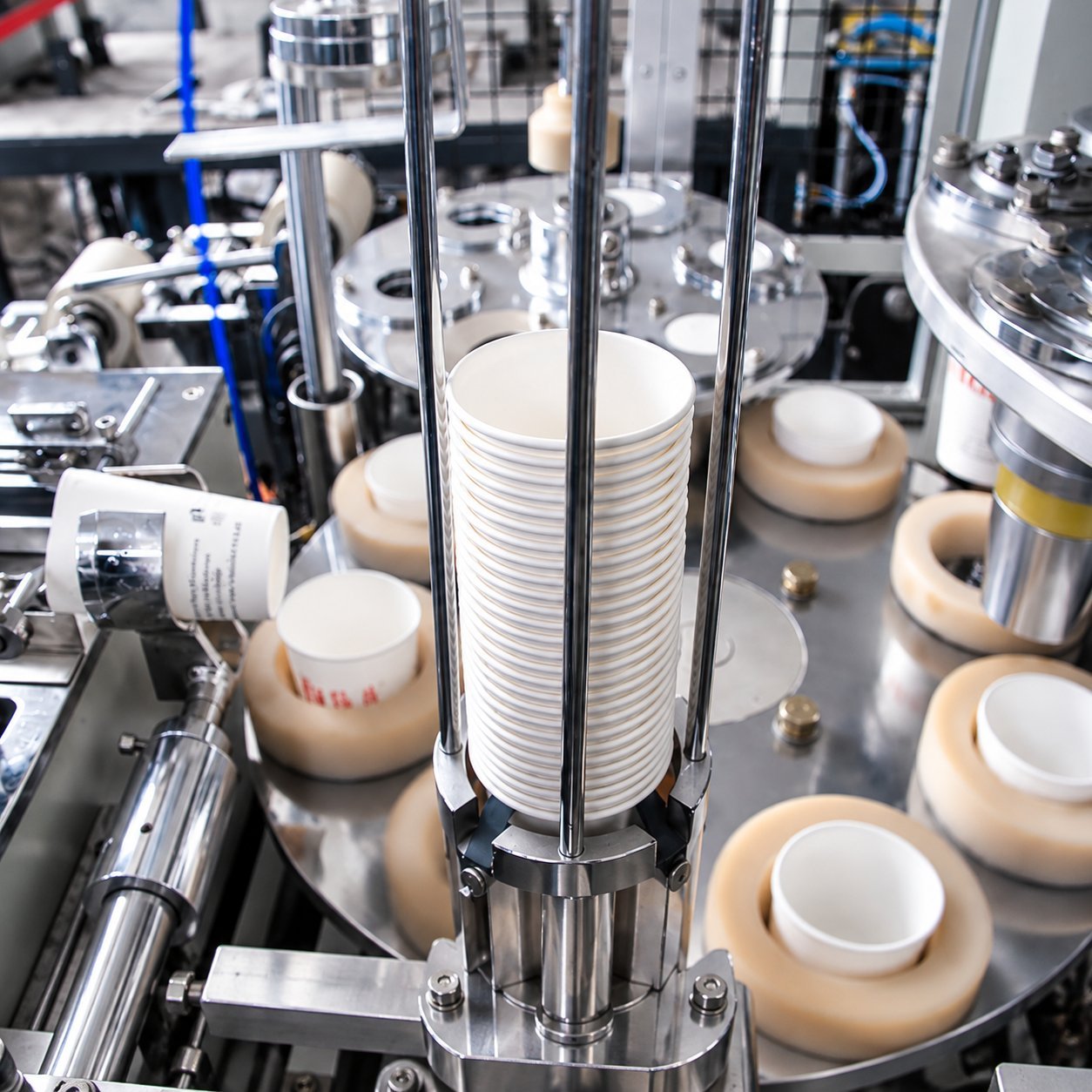 Close-up of a paper cup forming machine with stacked cups and precision tooling, illustrating in-process QC checkpoints.