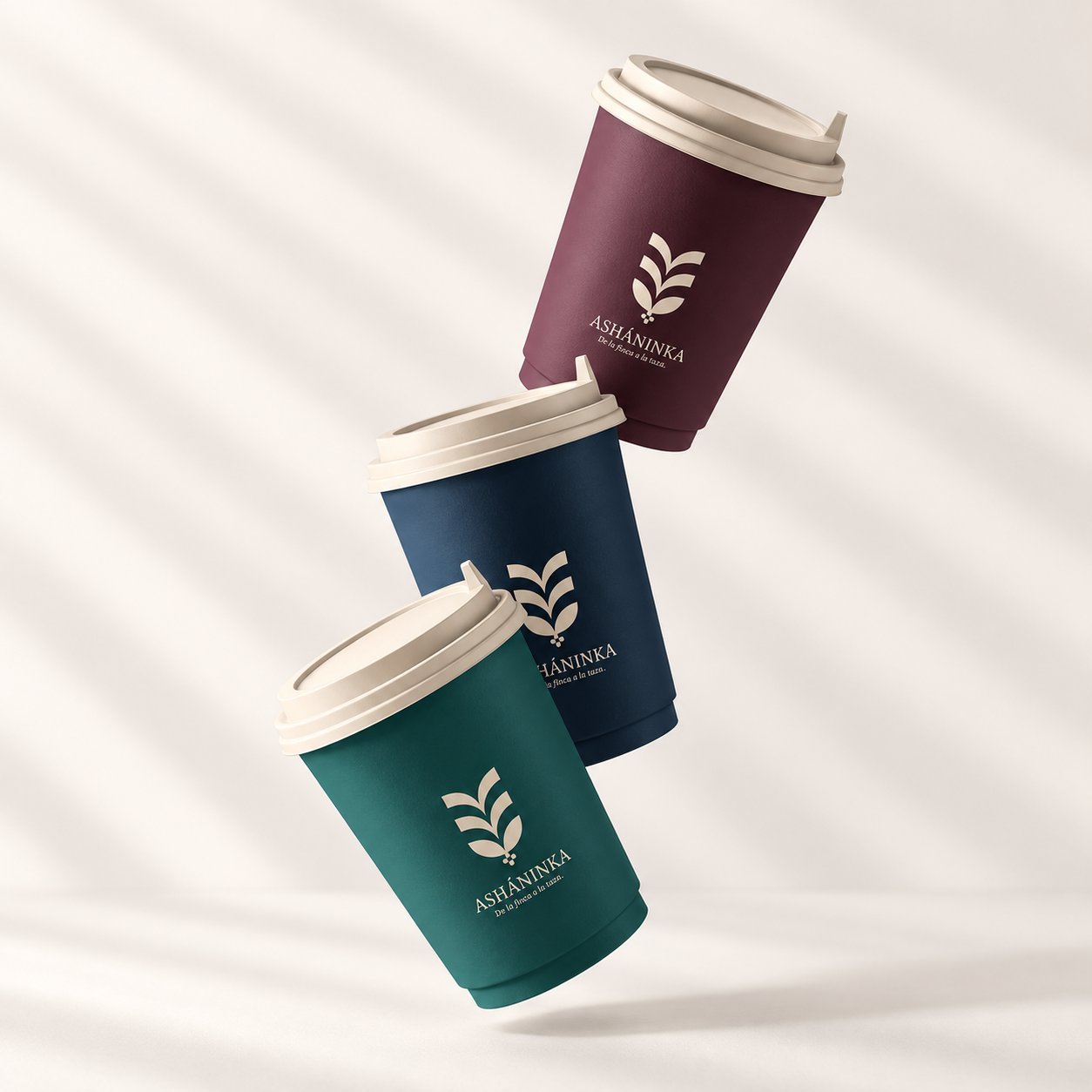 Three branded paper cups with lids in purple, navy and green ASHANINKA design, showing finished product at the packing and container-loading stage.