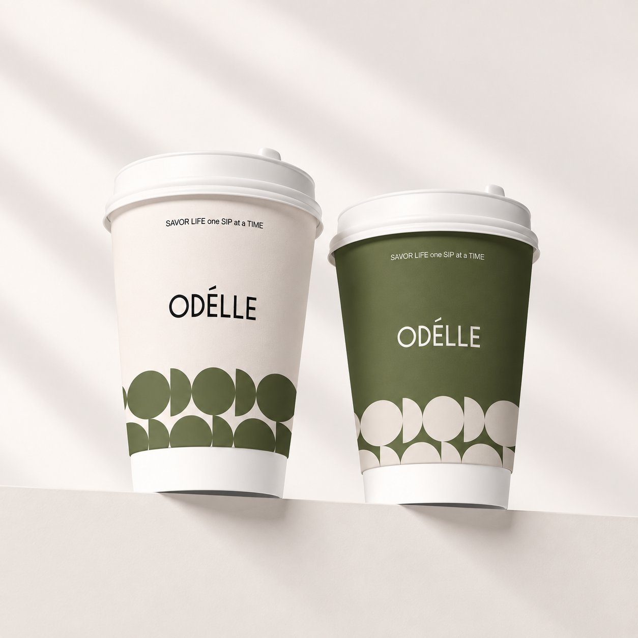 Two Odelle branded paper cups in white and green with the same circular print pattern, illustrating how one approved design is color-matched across variants.