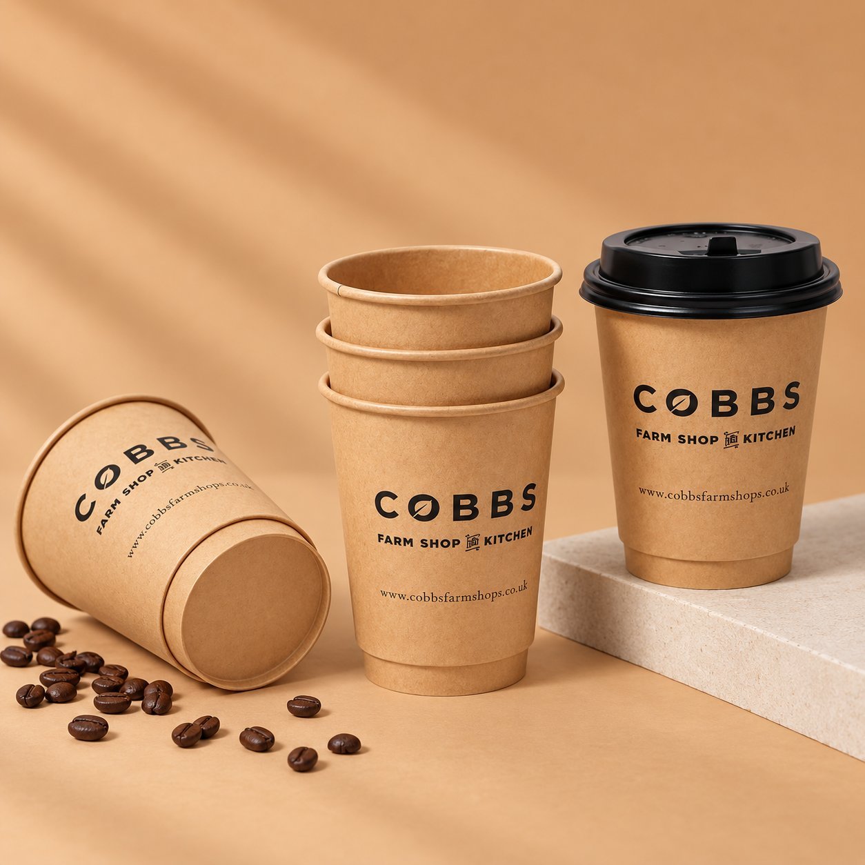 Kraft paper coffee cups in COBBS Farm Shop design, one with a black lid, showing double-wall construction with its own visual weight and finished look.
