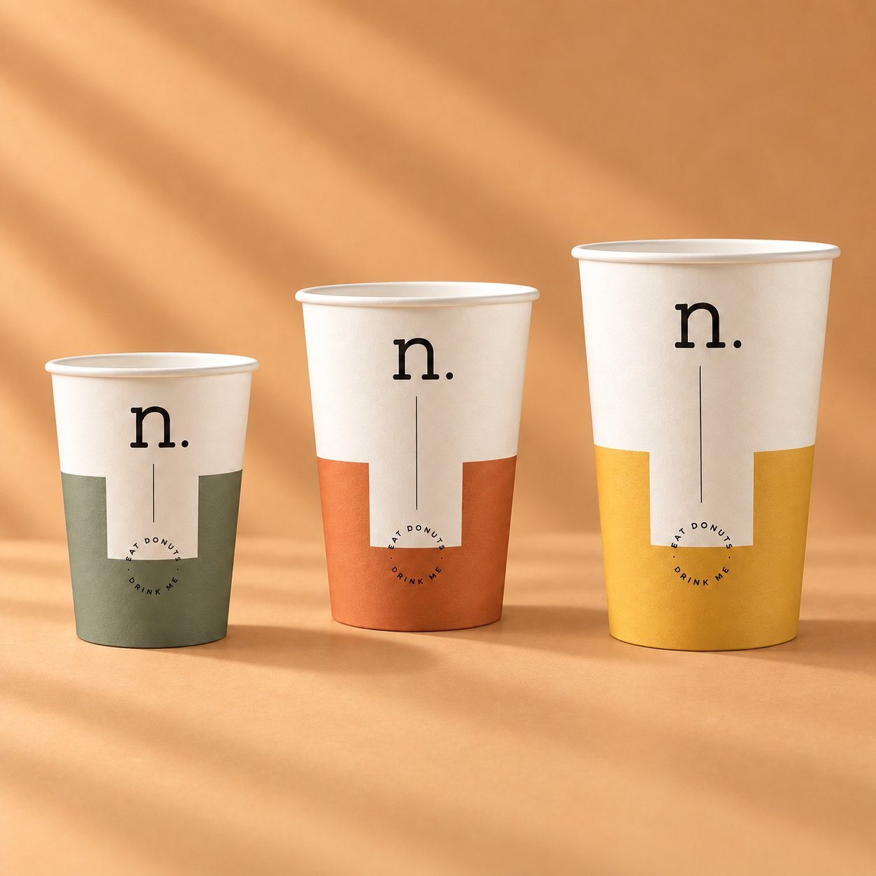 Three single-wall paper cups in n. brand Eat Donuts Drink Me design in three colorways and three sizes, showing the single-layer construction across a brand family.
