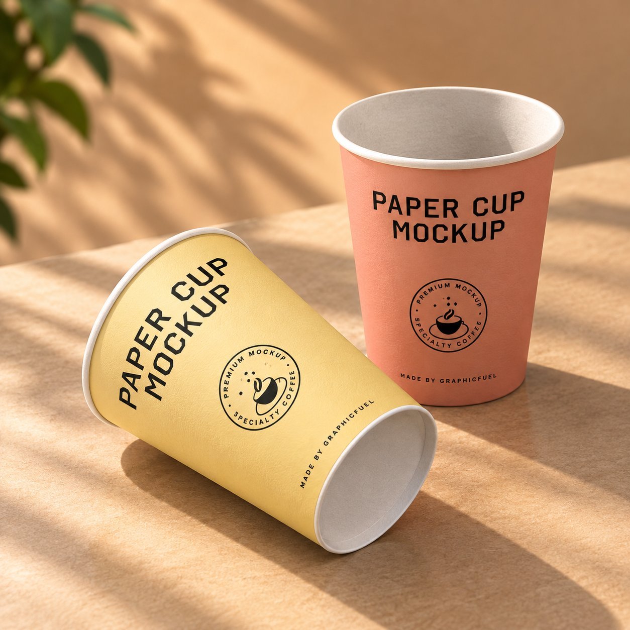 A coral pink paper cup and a yellow paper cup, both branded 'PAPER CUP MOCKUP' with a 'Premium Mockup Specialty Coffee' seal, resting on a kraft surface — a printed single- or double-side coated finish used for takeaway service.