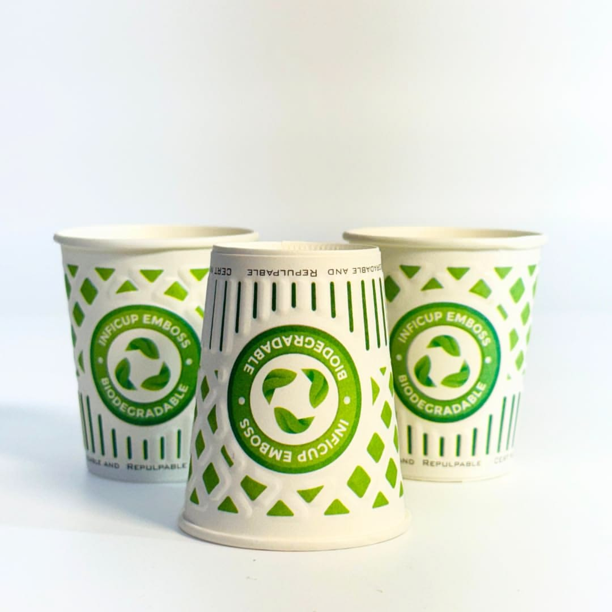 Three white paper cups with green printed graphics promoting 'Inficup Emboss' and 'Biodegradable' certification, set against a clean white surface — an example of finished retail cup marketing that visibly claims biodegradability, where the underlying compliance claims still need separate PFAS, heavy-metal, and Declaration of Conformity evidence under Regulation (EU) 2025/40.